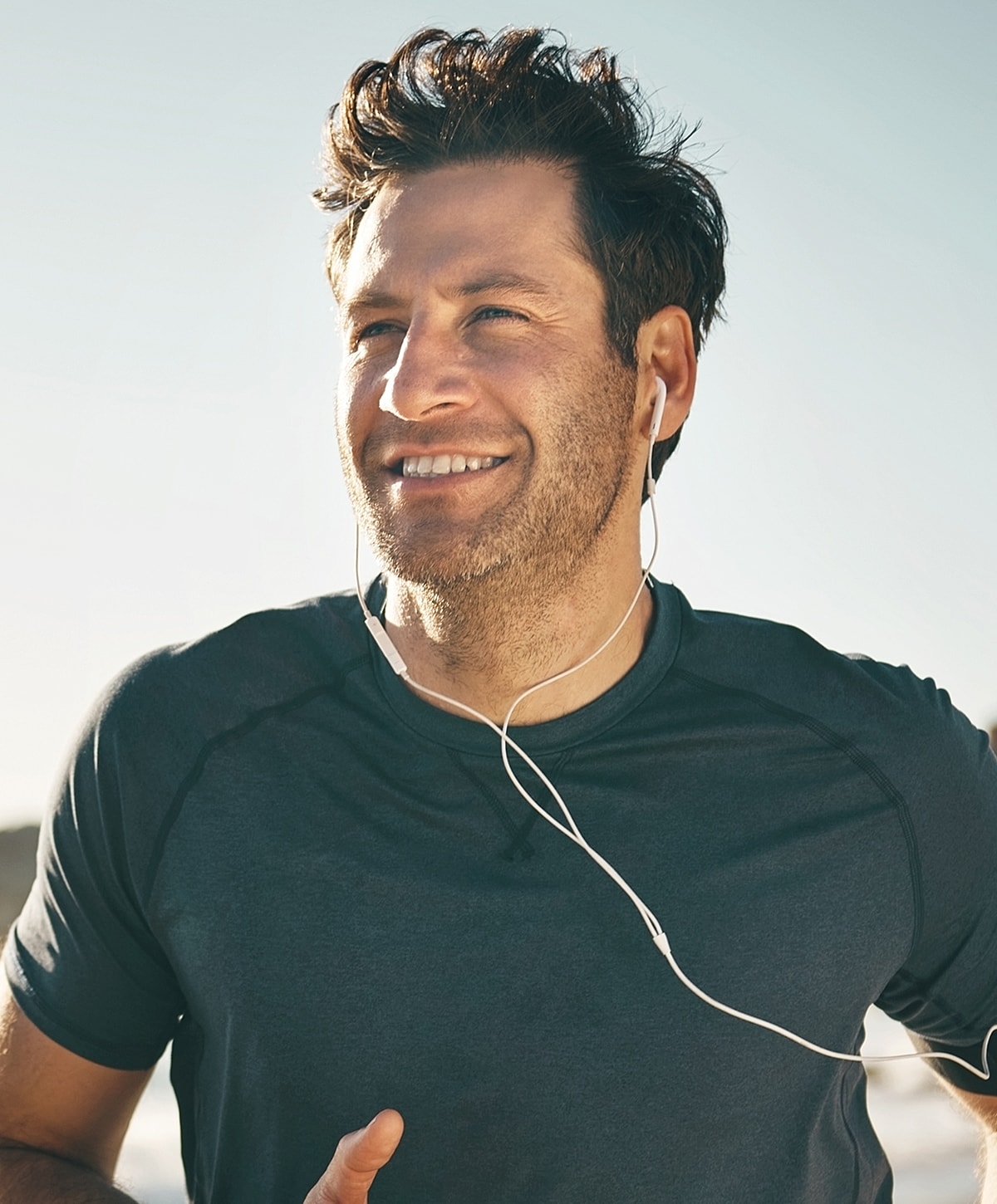 Man jogging with earphones and smiling outdoors.