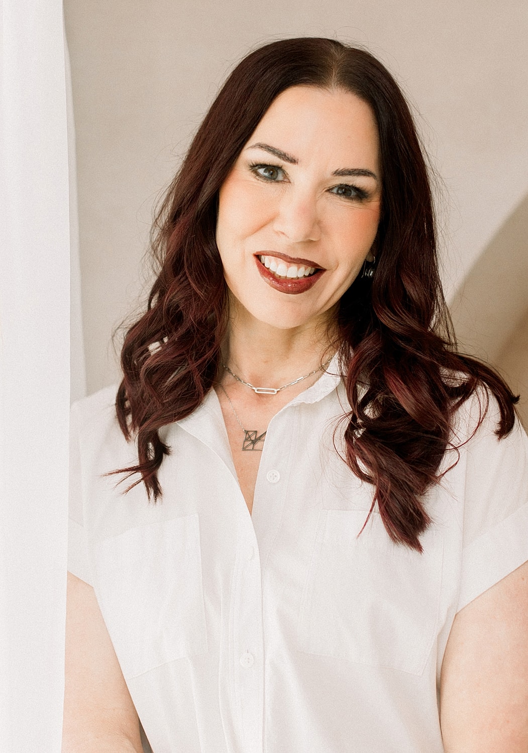 Woman smiling, wearing a white shirt indoors.