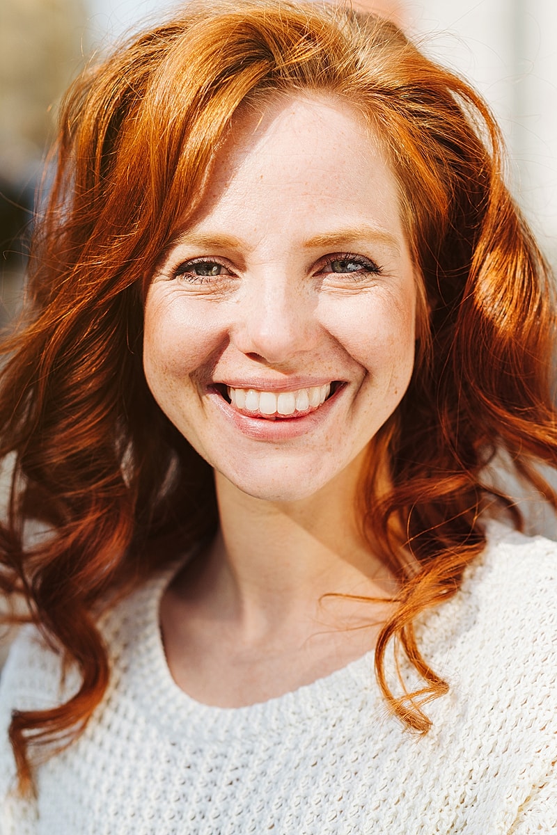 Smiling woman with red curly hair outdoors.