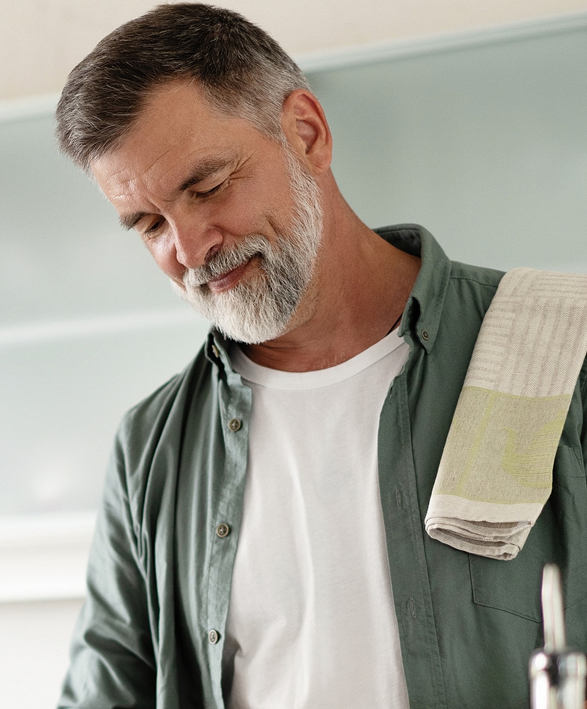 Smiling older man in kitchen with towel.