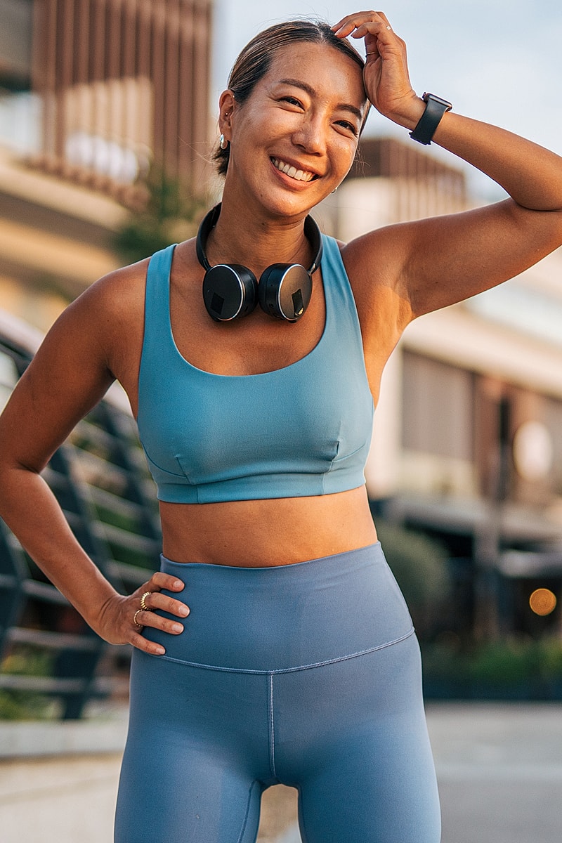 Smiling woman in workout clothes outdoors with headphones.