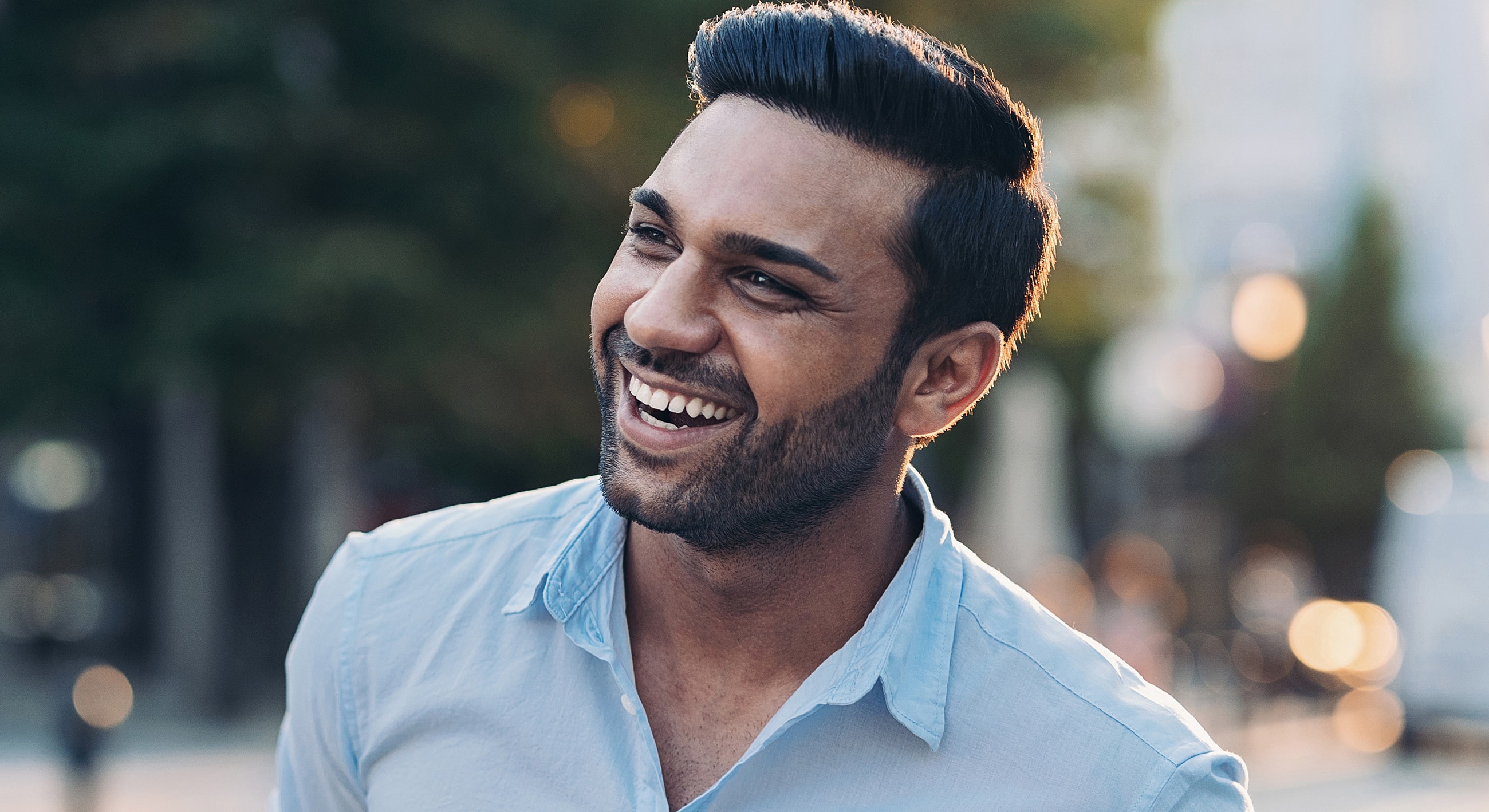 Smiling man in casual blue shirt outdoors.