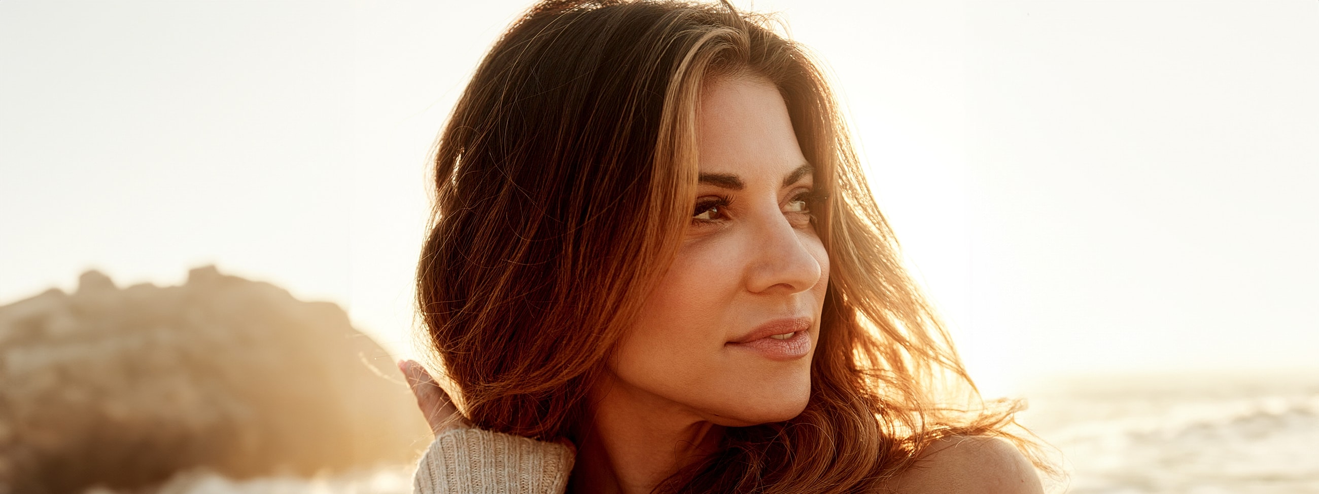 Woman with flowing hair by the beach at sunset.