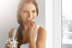 Beautiful woman with dark, braided hair smiles as she takes a weight loss pill