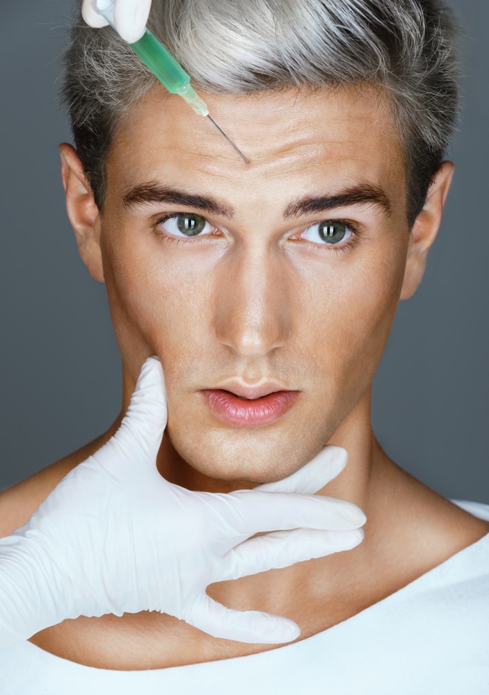 Handsome gray-haired man raises his eyebrows as his specialist administers forehead injections