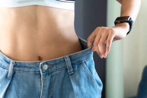 Woman holds her overly large old jeans up to her slender waist after losing weight during the holidays